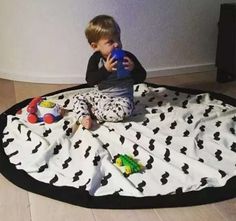 a little boy sitting on the floor drinking out of a cup and playing with his toys