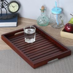 a wooden tray with a glass on it and an alarm clock in the back ground