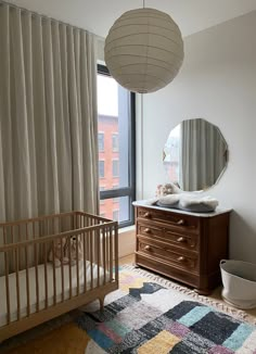 a baby's room with a crib, dresser and large window overlooking the city