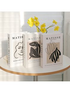 three books sitting on top of a table next to a vase filled with yellow flowers