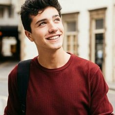 a smiling young man in a red sweater is standing on the street and looking up