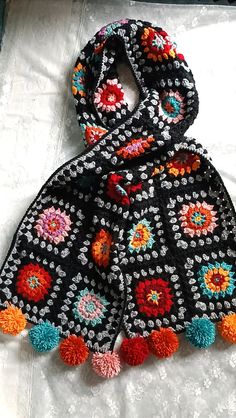 a black scarf with multicolored pom poms on it sitting on a bed