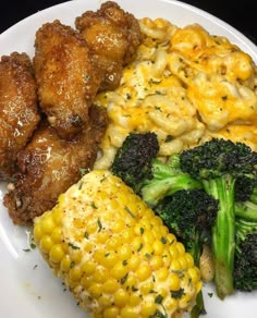 a white plate topped with chicken, broccoli and macaroni next to corn on the cob