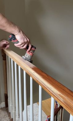 a man sanding the bottom of a banister rail with a stapler on it