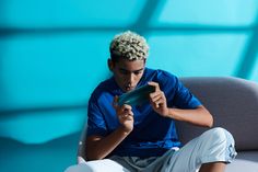 a young man sitting on a couch looking at his cell phone while holding something in his hand