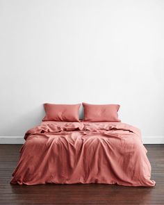 a bed with pink sheets and pillows in a white room next to a wooden floor