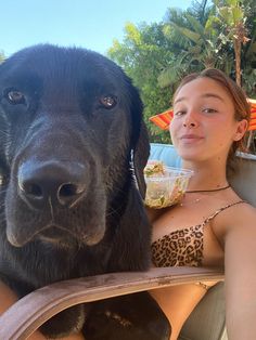 a woman sitting next to a black dog on top of a beach chair in the sun