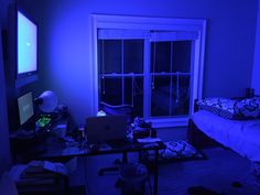 a room with a bed, desk and television in it at night time is lit up by blue light