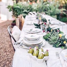 an outdoor table set with plates, bowls and succulents in white dishes