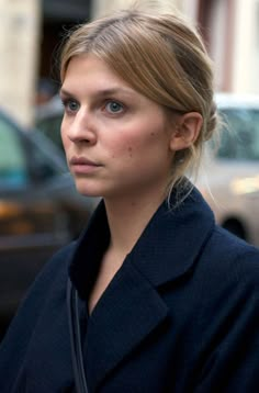 a woman standing in front of a car looking off to the side with a serious look on her face