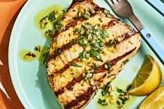 a piece of grilled fish on a blue plate with lemon wedges next to it