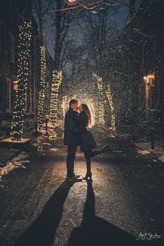 a man and woman standing in the middle of an alley at night with lights all around them