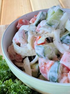 a bowl filled with pasta and vegetables on top of a wooden table next to parsley