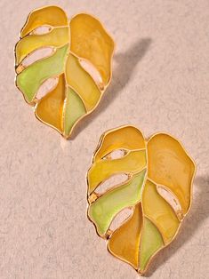 two yellow and green leaf shaped brooches sitting on top of a table next to each other