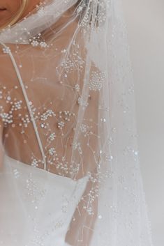 a woman wearing a wedding veil with beading on the bottom and neckline is looking down at her dress