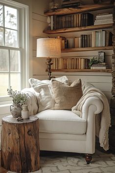 a white couch sitting in front of a window next to a table with books on it