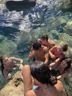 a group of young people standing in the water next to each other near rocks and boulders