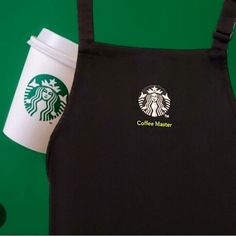 a starbucks coffee maker apron with a cup of coffee in front of it on a green background