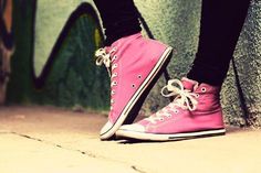 a person wearing pink converse shoes standing next to a wall