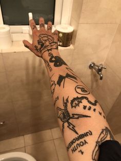 a person's arm with tattoos on it next to a toilet