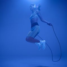 a woman jumping in the air with a jump rope and headphones on her ears