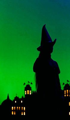 the silhouette of a person wearing a witches hat in front of a green and blue sky