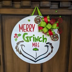 a merry grinmas sign hanging on a door with green and red bows attached to it