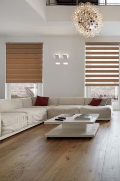 a modern living room with wood flooring and white couches, windows covered in blinds