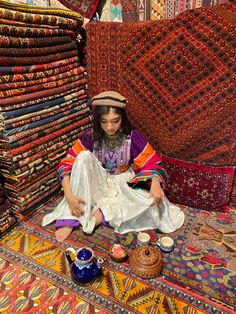 a woman sitting on the ground surrounded by rugs