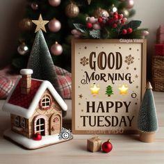 there is a small house next to a christmas tree and a sign that says good morning happy tuesday