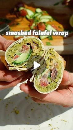 a person holding a sandwich in their hand with the words smashed falafel wrap