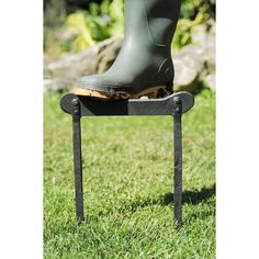 a pair of rubber boots sitting on top of a metal stand in the grass with one leg up