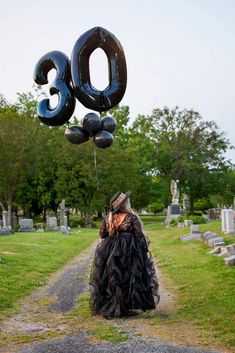 a woman in a black dress and hat holding an air filled number balloon