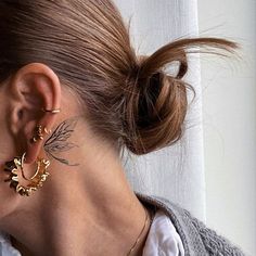 a close up of a person wearing gold earring and a white shirt with a window in the background