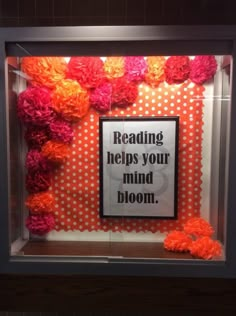 a sign that reads reading helps your mind bloom in front of a display case with orange and pink flowers