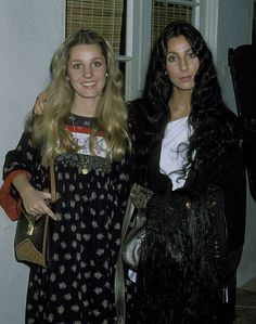 two women standing next to each other holding purses