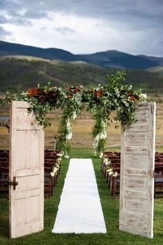 an open door leading to the aisle with flowers and greenery on it, in front of mountains