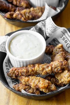 two trays filled with fried food next to a bowl of ranch dressing on a wooden table