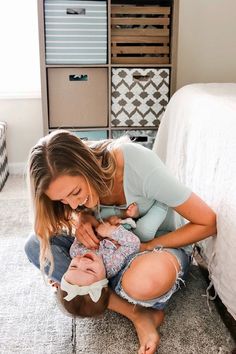 a woman holding a baby in her lap while sitting on the floor next to a bed