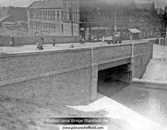 an old black and white photo of people walking on the side of a bridge over water