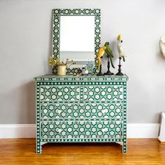 a green and white dresser sitting next to a mirror on top of a wooden floor