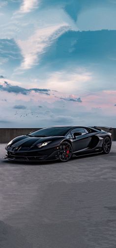 a black sports car parked on the side of an empty parking lot in front of a cloudy sky