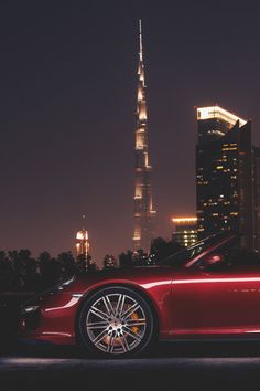 a red sports car parked in front of a tall building at night with the lights on