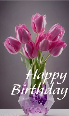 a vase filled with pink tulips sitting on top of a table next to a happy birthday sign