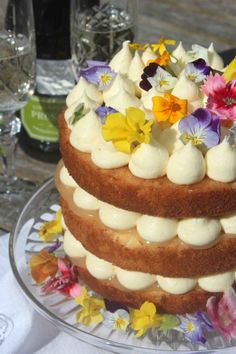 a three layer cake with white frosting and colorful flowers on the top is sitting on a glass plate