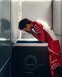 a man in a red and white racing suit leaning against a black box with water coming out of it