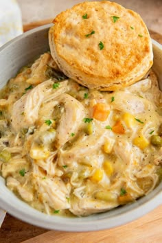 a bowl filled with chicken pot pie soup next to a biscuit on a cutting board