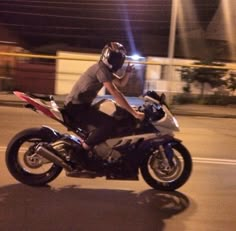 a man riding on the back of a motorcycle down a street at night with its lights on