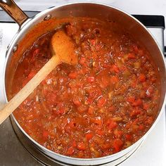 a pot full of stew with a wooden spoon on the stove top next to it