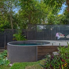 an outdoor hot tub in the middle of a fenced area with trees and plants